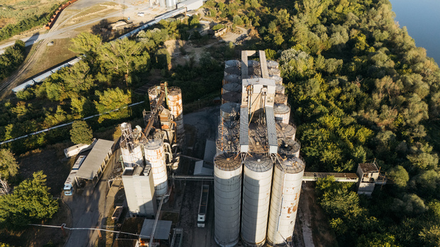 Aerial view of industrial grain silos with tall metal cylinders and processing structures surrounded by lush green trees near a river in Sremska Mitrovica Vojvodina Serbia. Aerial view of industrial grain silos with tall metal cylinders and processing structures surrounded by lush green trees near a river in Sremska Mitrovica Vojvodina Serbia.