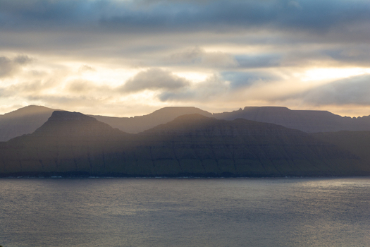 View of the dramatic mountains and cliffs of the Faroe Islands rising above the sea under a cloudy sky at sunset Faroe Islands. View of the dramatic mountains and cliffs of the Faroe Islands rising above the sea under a cloudy sky at sunset Faroe Islands.