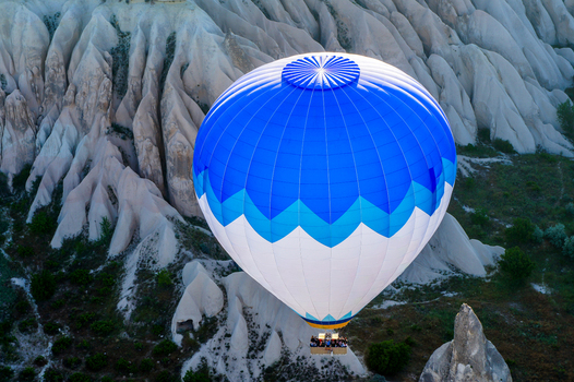 Aerial view of a blue and white hot air balloon with people in the basket flying over the unique rock formations and valleys of Cappadocia Kayseri Kayseri Turkiye. Aerial view of a blue and white hot air balloon with people in the basket flying over the unique rock formations and valleys of Cappadocia Kayseri Kayseri Turkiye.