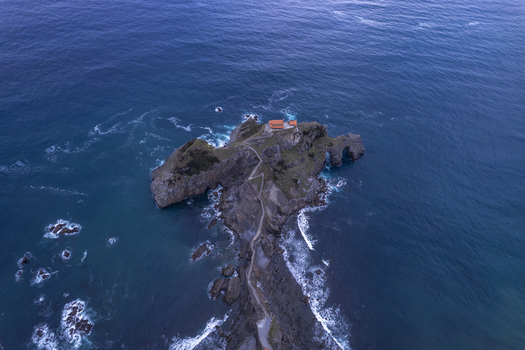 Aerial view of San Juan de Gaztelugatxe a historic hermitage on a rocky islet connected by a winding stone bridge surrounded by deep blue waters in Gaztelugatxeko Doniene Euskadi Spain.