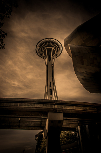 View of the Space Needle and the Museum of Pop Culture with the monorail track in the foreground under a dramatic cloudy sky in Seattle Washington United States.