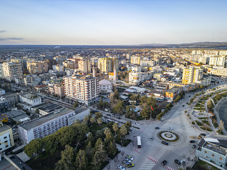 Aerial view of Sheshi Pavaresia in the city center of Fier featuring a roundabout surrounding urban buildings lush trees and clear daylight in Fier Qarku i Fierit Albania. Aerial view of Sheshi Pavaresia in the city center of Fier featuring a roundabout surrounding urban buildings lush trees and clear daylight in Fier Qarku i Fierit Albania.