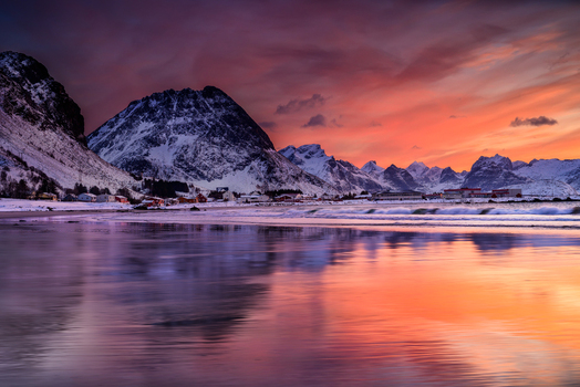 View of a snowy beach at sunset with dramatic mountains and reflections in the wet sand in Leknes Lofoten Norway.
