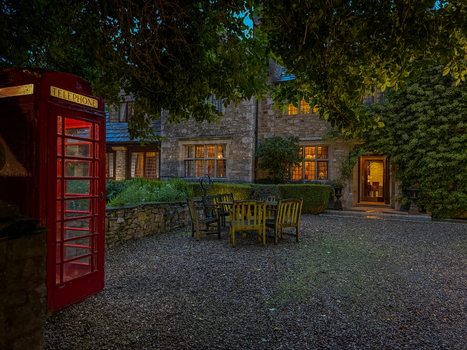 View of an illuminated red telephone booth and a historic stone building with glowing windows and outdoor seating in a gravel courtyard Hawes England United Kingdom. View of an illuminated red telephone booth and a historic stone building with glowing windows and outdoor seating in a gravel courtyard Hawes England United Kingdom.