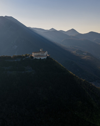Aerial view of the Santuario del Santissimo Salvatore perched on a mountain ridge surrounded by dense forests and distant peaks in Montella Campania Italy. Aerial view of the Santuario del Santissimo Salvatore perched on a mountain ridge surrounded by dense forests and distant peaks in Montella Campania Italy.