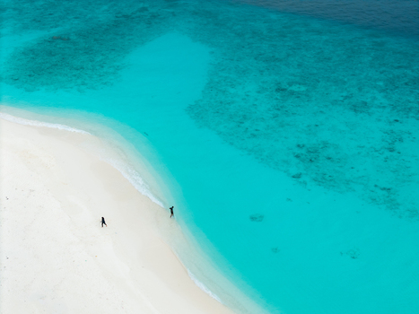Aerial view of turquoise waters meet the pristine white sands where tiny figures stroll along the shore Hoarafushi Thiladhunmathee Uthuruburi Maldives. Aerial view of turquoise waters meet the pristine white sands where tiny figures stroll along the shore Hoarafushi Thiladhunmathee Uthuruburi Maldives.