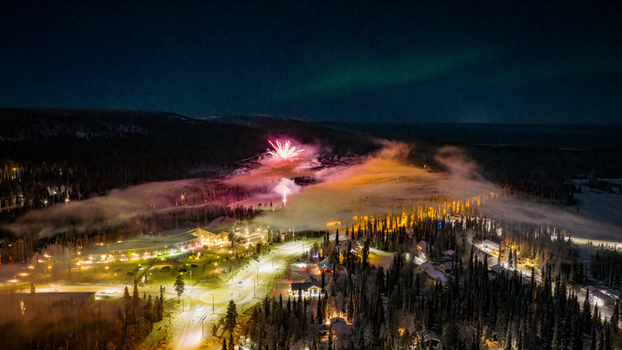 Aerial view of Luosto ski resort at night with fireworks exploding over snow covered forests and the aurora borealis in the sky Sodankyla Lapland Finland. Aerial view of Luosto ski resort at night with fireworks exploding over snow covered forests and the aurora borealis in the sky Sodankyla Lapland Finland.