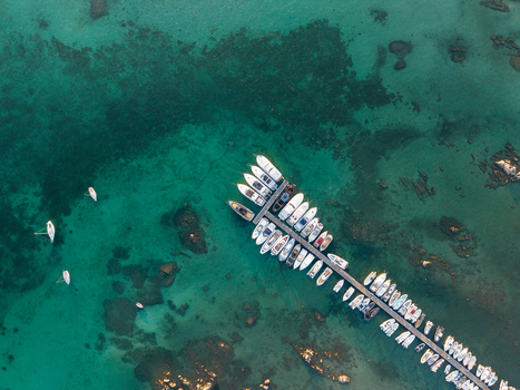 Aerial view of a long wooden pier crowded with white boats moored in the clear turquoise waters of the Mediterranean Sea with rocky seabed formations in Marinella Sardegna Italy. Aerial view of a long wooden pier crowded with white boats moored in the clear turquoise waters of the Mediterranean Sea with rocky seabed formations in Marinella Sardegna Italy.