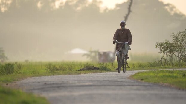 View of an elderly man riding a bicycle on a rural road Bangladesh.