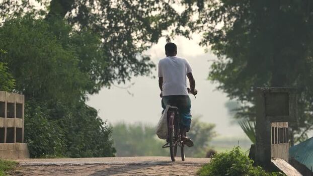 View of a man riding a bicycle on a rural road Bangladesh.