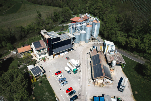 Aerial view of Moulin de la Vaux industrial facility with silver silos solar panels on rooftops and a parking lot surrounded by lush green trees in Aubonne Vaud Switzerland. Aerial view of Moulin de la Vaux industrial facility with silver silos solar panels on rooftops and a parking lot surrounded by lush green trees in Aubonne Vaud Switzerland.