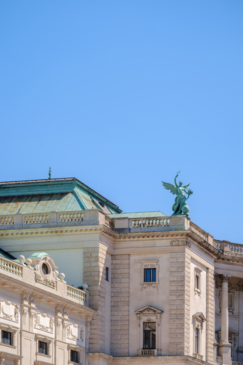 View of the Hofburg palace featuring its ornate stone facade green copper roof and a winged statue against a clear blue sky in Vienna Vienna Austria. View of the Hofburg palace featuring its ornate stone facade green copper roof and a winged statue against a clear blue sky in Vienna Vienna Austria.