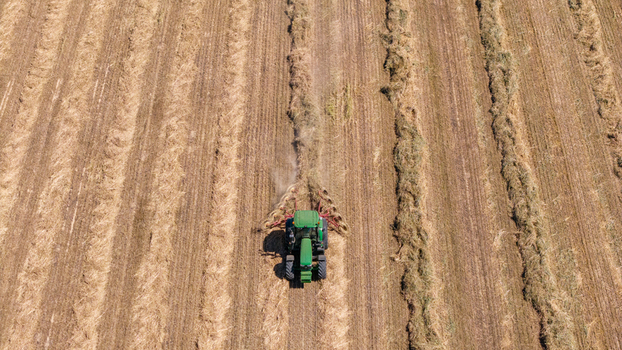 Aerial view of a green tractor harvesting hay in a field with rows of cut grass in Philadelphia Western Cape South Africa. Aerial view of a green tractor harvesting hay in a field with rows of cut grass in Philadelphia Western Cape South Africa.