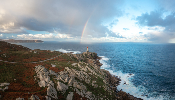 Aerial view of Faro de Punta Nariga with a rainbow arching over the lighthouse rugged rocky cliffs and the Atlantic Ocean under a cloudy sky Malpica A Coruna Spain. Aerial view of Faro de Punta Nariga with a rainbow arching over the lighthouse rugged rocky cliffs and the Atlantic Ocean under a cloudy sky Malpica A Coruna Spain.