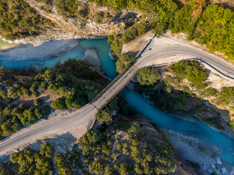 Aerial view of Osumi Canyon featuring a bridge spanning the turquoise river surrounded by lush green trees and steep rocky cliffs in Dhores Berat County Albania.