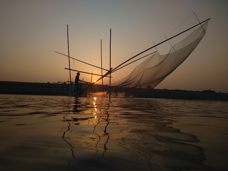 View of a fisherman using a traditional lift net on the river at sunset in Kushtia Khulna Division Bangladesh. View of a fisherman using a traditional lift net on the river at sunset in Kushtia Khulna Division Bangladesh.