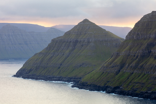 View of the dramatic green mountains and rocky coastline of the Faroe Islands. View of the dramatic green mountains and rocky coastline of the Faroe Islands.