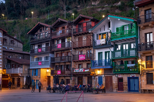 Pasai Donibane Spain 09 March 2026 View of traditional houses with colorful wooden balconies and people sitting at outdoor cafe tables at dusk in the historic harbor street.