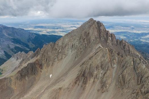 Aerial view of Mount Sneffels in the San Juan Mountains with rugged rocky slopes jagged peaks and a cloudy sky in Ouray County Colorado United States. Aerial view of Mount Sneffels in the San Juan Mountains with rugged rocky slopes jagged peaks and a cloudy sky in Ouray County Colorado United States.