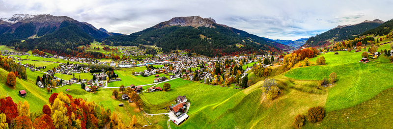 Aerial view of Klosters Serneus nestled in the Grisons Alps featuring traditional chalets autumn foliage green pastures and mountain peaks in Klosters Serneus Grisons Switzerland.