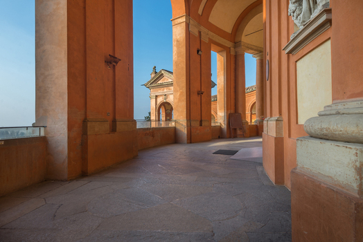 View of the portico and arches of the Santuario Madonna di San Luca with warm terracotta walls and stone flooring under a clear blue sky Bologna Emilia Romagna Italy. View of the portico and arches of the Santuario Madonna di San Luca with warm terracotta walls and stone flooring under a clear blue sky Bologna Emilia Romagna Italy.