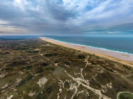Aerial view of Dunes de Biville featuring expansive sand dunes winding paths and the coastline meeting the Atlantic Ocean under a cloudy sky in La Hague Normandie France.