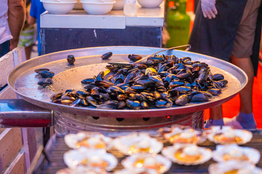 View of glistening mussels piled high on a large metal platter juxtaposed with rows of scallop shells creating a feast for the eyes Pula Istria County Croatia.
