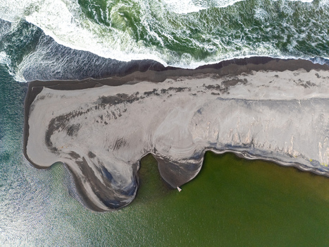 Aerial view of Depok Beach showing dark volcanic sand crashing ocean waves and the calm green waters of the lagoon in the Special Region of Yogyakarta Indonesia. Aerial view of Depok Beach showing dark volcanic sand crashing ocean waves and the calm green waters of the lagoon in the Special Region of Yogyakarta Indonesia.