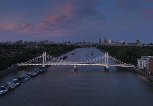 Aerial view of the illuminated Albert Bridge spanning the River Thames at dusk with the city skyline in the background in London Greater London United Kingdom.