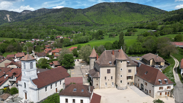 Aerial view of the historic Chateau De Vesancy with its round towers and the adjacent village church against a backdrop of lush green mountains in Vesancy Auvergne Rhone Alpes France. Aerial view of the historic Chateau De Vesancy with its round towers and the adjacent village church against a backdrop of lush green mountains in Vesancy Auvergne Rhone Alpes France.