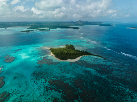 Aerial view of a vivid turquoise lagoon embracing a small lush island with a pristine beach contrasting against the deep blue sea Noumea New Caledonia. Aerial view of a vivid turquoise lagoon embracing a small lush island with a pristine beach contrasting against the deep blue sea Noumea New Caledonia.
