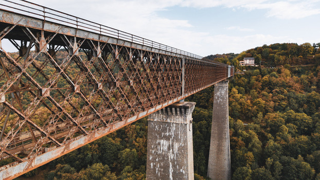 Aerial view of the historic Fades viaduct with its rusty iron truss structure and stone piers spanning over a dense forest in Les Ancizes Comps Auvergne Rhone Alpes France. Aerial view of the historic Fades viaduct with its rusty iron truss structure and stone piers spanning over a dense forest in Les Ancizes Comps Auvergne Rhone Alpes France.