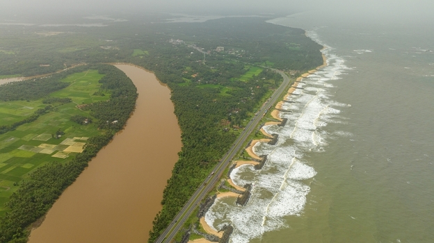 Aerial view of Maravanthe beach with a road separating the Arabian Sea and the Souparnika River surrounded by lush green fields and coastal waves in Maravanthe Karnataka India. Aerial view of Maravanthe beach with a road separating the Arabian Sea and the Souparnika River surrounded by lush green fields and coastal waves in Maravanthe Karnataka India.