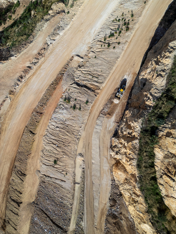 Aerial view of an open pit mine with heavy machinery operating on dirt roads and steep excavated rock walls in Teulada Valencian Community Spain.