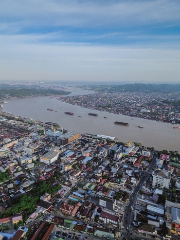 Aerial view of the Mahakam River flowing through Samarinda featuring dense urban rooftops a mosque and cargo barges on the water in Samarinda Kalimantan Timur Indonesia. Aerial view of the Mahakam River flowing through Samarinda featuring dense urban rooftops a mosque and cargo barges on the water in Samarinda Kalimantan Timur Indonesia.