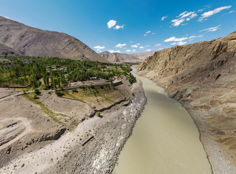 Aerial view of the Indus River flowing through a rugged mountain valley with lush green trees and rocky terrain in Ladakh Division Ladakh India. Aerial view of the Indus River flowing through a rugged mountain valley with lush green trees and rocky terrain in Ladakh Division Ladakh India.