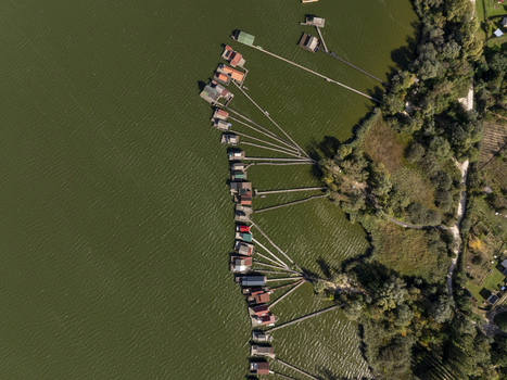Aerial view of Bokodi Floating Village featuring colorful wooden houses on stilts connected by long wooden walkways over the green lake water in Oroszlany Hungary. Aerial view of Bokodi Floating Village featuring colorful wooden houses on stilts connected by long wooden walkways over the green lake water in Oroszlany Hungary.