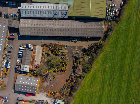 Aerial view of Ladfordfields Industrial Estate featuring industrial warehouses metal scrap storage parked vehicles and adjacent green fields in Stafford England United Kingdom. Aerial view of Ladfordfields Industrial Estate featuring industrial warehouses metal scrap storage parked vehicles and adjacent green fields in Stafford England United Kingdom.