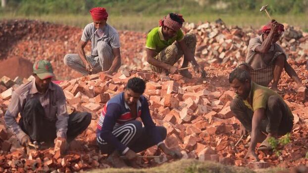 View of men working in a brickyard breaking red bricks Bangladesh.