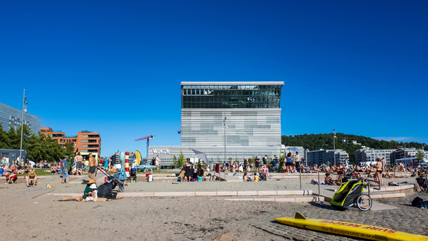 Oslo Norway 24 June 2024 View of the Munch Museum with people sunbathing on the sandy beach under a clear blue sky.