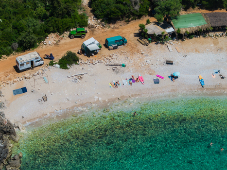Aerial view of Aquarium Beach featuring turquoise waters white pebbles camper vans parked on the shore and people sunbathing in Jala Vlore County Albania. Aerial view of Aquarium Beach featuring turquoise waters white pebbles camper vans parked on the shore and people sunbathing in Jala Vlore County Albania.