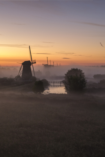 Aerial view of the historic windmills of Kinderdijk silhouetted against a golden sunrise sky with thick morning mist over the water Kinderdijk Zuid Holland Netherlands.