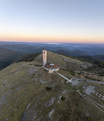Aerial view of the abandoned Buzludzha Monument perched on a mountain peak at sunset with rolling hills and a clear sky in the background in Stara Zagora Bulgaria. Aerial view of the abandoned Buzludzha Monument perched on a mountain peak at sunset with rolling hills and a clear sky in the background in Stara Zagora Bulgaria.