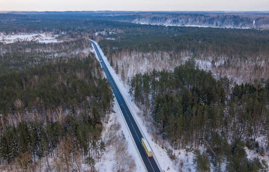 Aerial view of a straight asphalt road cutting through a dense snow covered pine forest with a truck and cars in winter Lithuania. Aerial view of a straight asphalt road cutting through a dense snow covered pine forest with a truck and cars in winter Lithuania.