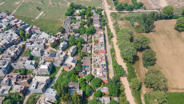Lahore Pakistan 08 September 2026 Aerial view of a residential neighborhood featuring dense housing flat rooftops lush green trees and adjacent agricultural fields.