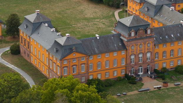 Aerial view of the historic Schloss Lowenstein with its distinctive orange facade slate roofs and surrounding green parkland in Kleinheubach Bayern Germany. Aerial view of the historic Schloss Lowenstein with its distinctive orange facade slate roofs and surrounding green parkland in Kleinheubach Bayern Germany.