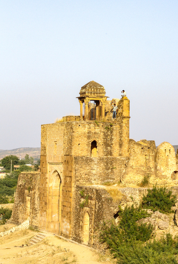 View of the historic Rohtas Fort with its ancient stone walls and towers featuring two people standing on the ramparts under a clear sky in Dina Punjab Pakistan. View of the historic Rohtas Fort with its ancient stone walls and towers featuring two people standing on the ramparts under a clear sky in Dina Punjab Pakistan.