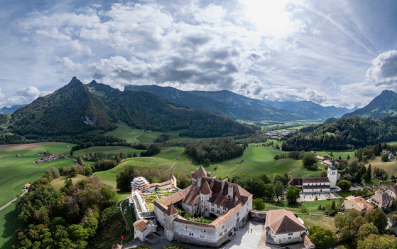 Aerial view of Chateau de Gruyeres surrounded by lush green hills forests and the Swiss Alps in Gruyeres Fribourg Switzerland. Aerial view of Chateau de Gruyeres surrounded by lush green hills forests and the Swiss Alps in Gruyeres Fribourg Switzerland.