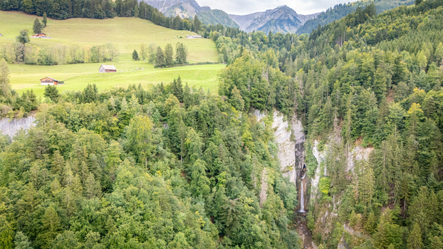 Aerial view of Grandvillard Waterfall cascading down a rocky cliff surrounded by dense green forest and alpine meadows Grandvillard Fribourg Switzerland.