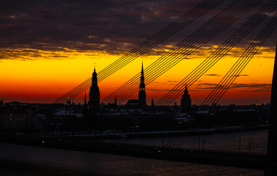 Aerial view of the Vansu Bridge with the silhouette of Old Riga skyline featuring church spires against a vibrant golden hour sunset over the Daugava River in Riga Latvia.